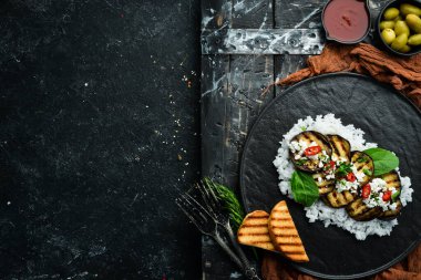 Siyah tabakta pilav ve peynirle kızartılmış patlıcan. Üst Manzara. Kırsal biçim.