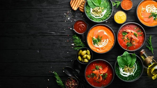 Set of colored soups. Spinach soup, tomato cream soup and carrot puree soup. Healthy food. On a black stone background.