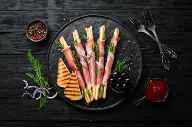 İtalyan Antipasto. Siyah tabakta jambonlu Grissini ekmeği. Kırsal tarzda. Üst Manzara. Metnin için boş yer.