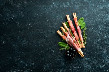 Jambonlu jambon ve Grissini ekmeği. Siyah taştan bir arka planda. Üst görünüm.