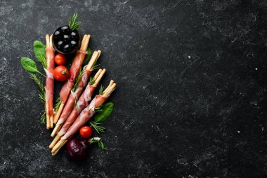 Jambonlu jambon ve Grissini ekmeği. Siyah taştan bir arka planda. Üst görünüm.
