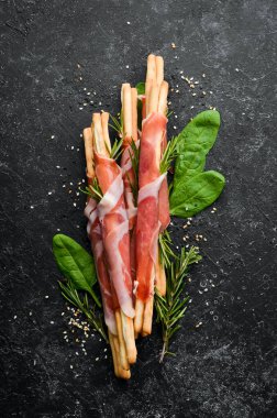 Jambonlu jambon ve Grissini ekmeği. Siyah taştan bir arka planda. Üst görünüm.