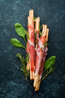 Jambonlu jambon ve Grissini ekmeği. Siyah taştan bir arka planda. Üst görünüm.