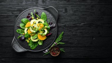 Portakallı taze vegan avokado salatası ve siyah tabakta ıspanak. Kırsal tarzda. Üst Manzara. Metnin için boş yer.