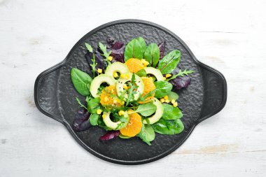 Portakallı taze vegan avokado salatası ve siyah tabakta ıspanak. Kırsal tarzda. Üst Manzara. Metnin için boş yer.