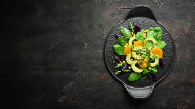 Portakallı taze vegan avokado salatası ve siyah tabakta ıspanak. Kırsal tarzda. Üst Manzara. Metnin için boş yer.
