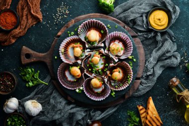 Deniz kabuklarında pişirilmiş deniz tarakları, sarımsak ve baharatlarla birlikte siyah taş bir tabakta. Deniz ürünleri. Üst Manzara. Metin için boş alan.