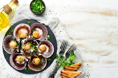 Deniz kabuklarında pişirilmiş deniz tarakları, sarımsak ve baharatlarla birlikte siyah taş bir tabakta. Deniz ürünleri. Üst Manzara. Metin için boş alan.