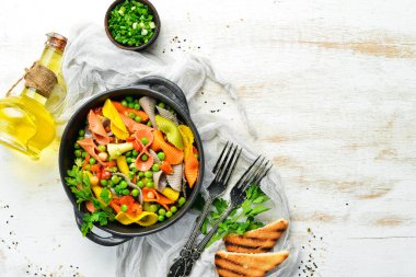 Siyah bir kasede bezelye ve sebzeli renkli makarna. Üst Manzara. Metin için boş alan.