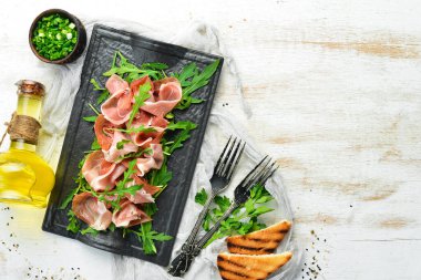 Jamon ve roka siyah bir taş tabakta. Prosciutto. Üst Manzara. Metin için boş alan.