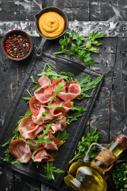 Jamon ve roka siyah bir taş tabakta. Prosciutto. Üst Manzara. Metin için boş alan.