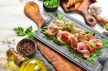 Jamon ve roka siyah bir taş tabakta. Prosciutto. Üst Manzara. Metin için boş alan.