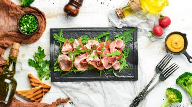 Jamon ve roka siyah bir taş tabakta. Prosciutto. Üst Manzara. Metin için boş alan.