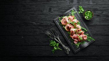Jamon ve roka siyah bir taş tabakta. Prosciutto. Üst Manzara. Metin için boş alan.