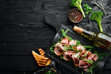 Jamon ve roka siyah bir taş tabakta. Prosciutto. Üst Manzara. Metin için boş alan.