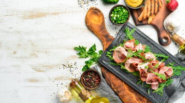 Jamon ve roka siyah bir taş tabakta. Prosciutto. Üst Manzara. Metin için boş alan.