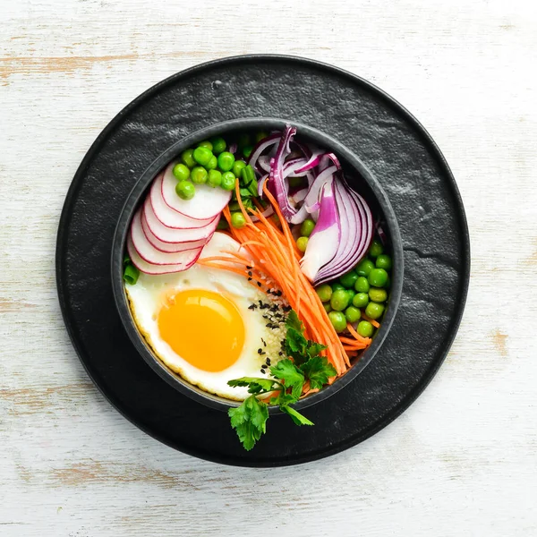 Buddha bowl: egg, green peas, onion, radish and carrots in a black stone bowl.