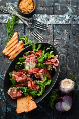 Siyah kasede zeytinli jambonlu salata. İspanyol mutfağı. Üst Manzara. Metnin için boş yer. Kırsal biçim.