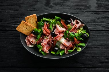 Siyah kasede zeytinli jambonlu salata. İspanyol mutfağı. Üst Manzara. Metnin için boş yer. Kırsal biçim.