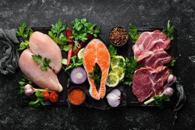 Et seti. Balık biftek, dana biftek ve tavuk göğsü. Üst Manzara. Siyah taştan bir arka planda.