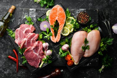 Et seti. Balık biftek, dana biftek ve tavuk göğsü. Üst Manzara. Siyah taştan bir arka planda.