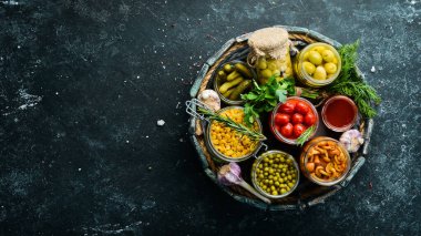 Sebze turşusu ve mantarlar siyah taş arka planda, tahta kutuda cam kavanozlarda. Üst görünüm.