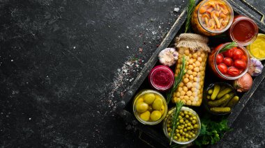 Sebze turşusu ve mantarlar siyah taş arka planda, tahta kutuda cam kavanozlarda. Üst görünüm.