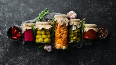 Cam kavanozlarda konserve sebze ve mantar seti. Siyah taş arka planda turşulu yiyecekler. Üst görünüm.
