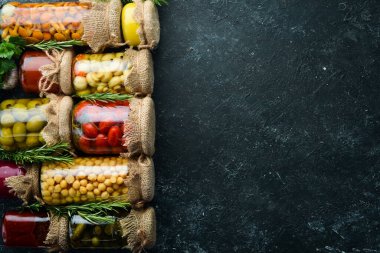 Cam kavanozlarda konserve sebze ve mantar seti. Siyah taş arka planda turşulu yiyecekler. Üst görünüm.