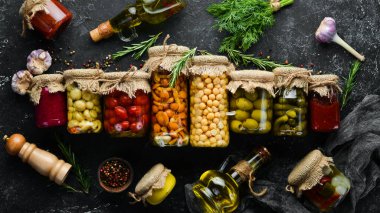 Cam kavanozlarda konserve sebze ve mantar seti. Siyah taş arka planda turşulu yiyecekler. Üst görünüm.