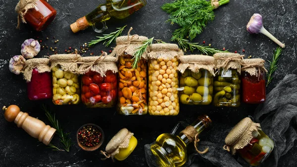 Cam kavanozlarda konserve sebze ve mantar seti. Siyah taş arka planda turşulu yiyecekler. Üst görünüm.