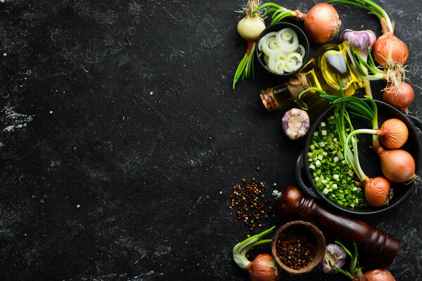 Culinary background. Onions, garlic and spices on a black stone background. Top view.