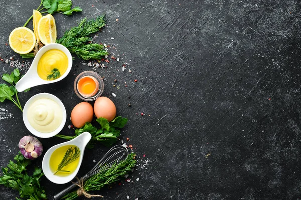 Mayonez sosu pişiriyorum. Yağ, hardal ve yumurta. Mutfak siyah taş arka planı. Üst görünüm.
