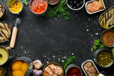 Konserve sebze, fasulye, balık ve meyveler siyah taş arka planda teneke kutularda. Yiyecek stokları.