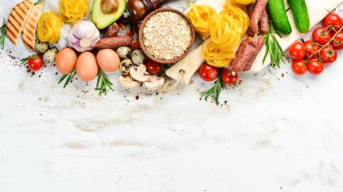 Beyaz ahşap gıda arka planı: domates, makarna, baharat, sebze ve sosis. Üst görünüm.
