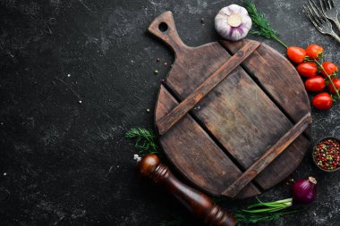 Kara mutfak geçmişi. Mutfak tahtası, sebzeler ve baharatlar siyah taş arka planda. Üst görünüm.