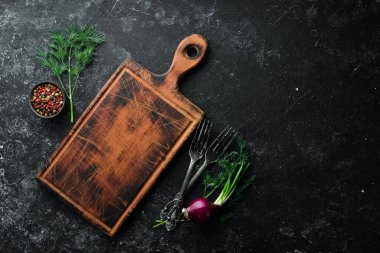 Kara mutfak geçmişi. Mutfak tahtası, sebzeler ve baharatlar siyah taş arka planda. Üst görünüm.