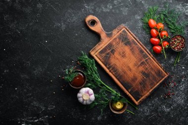 Kara mutfak geçmişi. Mutfak tahtası, sebzeler ve baharatlar siyah taş arka planda. Üst görünüm.