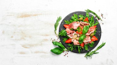 Siyah taş tabakta roka, prosciutto, çilek ve kapari salatası. İtalyan mutfağı.
