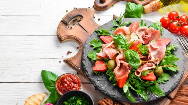 Siyah taş tabakta roka, prosciutto, çilek ve kapari salatası. İtalyan mutfağı.