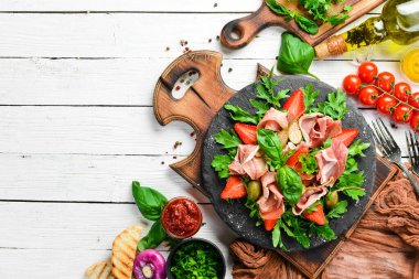 Siyah taş tabakta roka, prosciutto, çilek ve kapari salatası. İtalyan mutfağı.