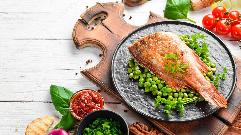 Baked sea red perch with green peas on a black stone plate. Top view. Free copy space.