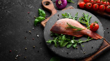 Çiğ deniz kırmızı levreği, biberiye ve siyah tabakta baharatlar. Deniz ürünleri. Üst Manzara. Metnin için boş yer.