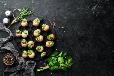 Fransız yemeği. Siyah taş zemin üzerinde pesto soslu fırında salyangoz. Üst Manzara. Metnin için boş yer.