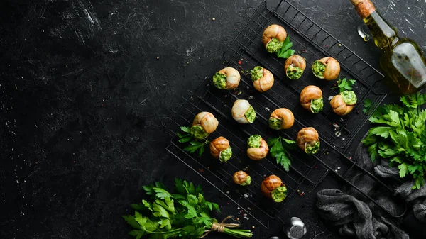 French food. Baked snails with pesto sauce on a black stone background. Top view. Free space for your text.