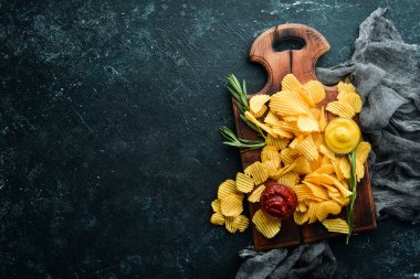 Ketçap ve hardal soslu patates cipsi. Siyah taşlı arka planda bira atıştırmalıkları. Üst görünüm.