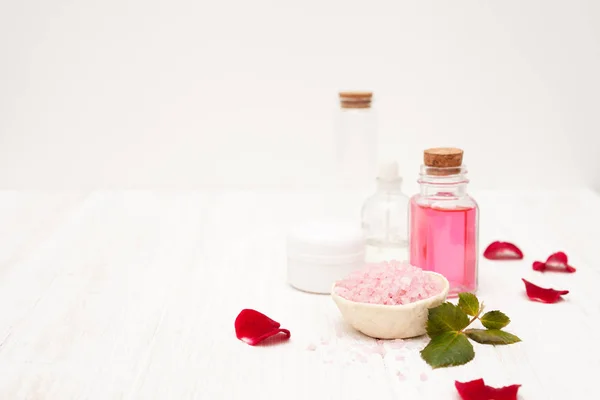 Соль, розовая вода из лепестков роз с руками на белом ву — стоковое фото