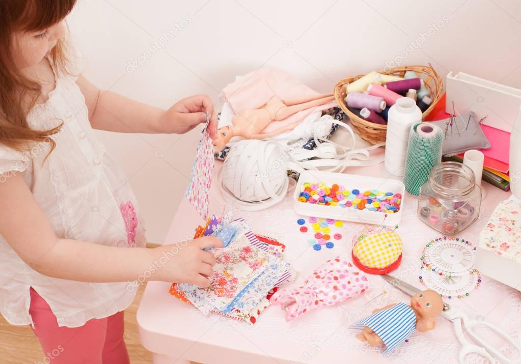 Girl sews dress dolls from pieces of fabric