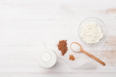 Kakao, tarçın, süzme peynir, bir şişede süt ve bir masanın üzerine şeker