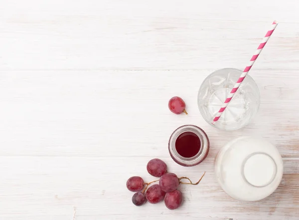 Kırmızı üzüm, süt şişesi ve şurubu beyaz bir tablo — Stok fotoğraf